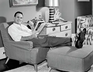 Oldtime Prints: 1950s RELAXED MAN SITTING IN EASY CHAIR FEET UP SMOKING PIPE READING MAGAZINE LOOKING AT CAMERA
