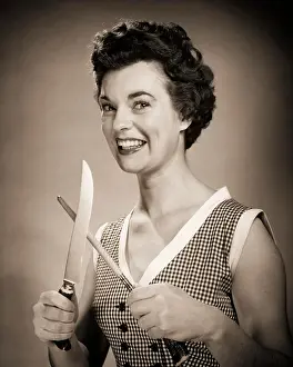 Knife Prints: 1950s SMILING EAGER WOMAN HOUSEWIFE HOLDING SHARPENING CARVING KNIFE LOOKING AT CAMERA