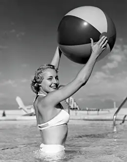 Bikini Prints: 1950S Side View Of Blonde In White Bikini Standing In Pool In Waist-High Water Holding Beach Ball In Air