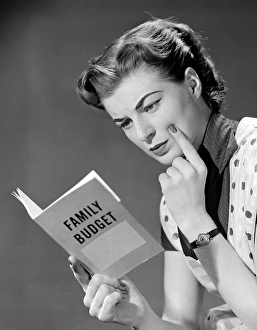 People Adults Prints: 1950S Woman In Apron Finger On Cheek Looking At Family Budget Book