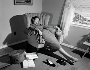 Oldtime Prints: 1950s WOMAN EXHAUSTED FROM SHOPPING SLUMPING IN LIVING ROOM CHAIR SHOES OFF PACKAGES EVERYWHERE LOOKING AT CAMERA