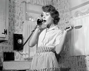 Communications Prints: 1950S Woman In Kitchen Wearing Apron Holding Spoon Talking On Telephone