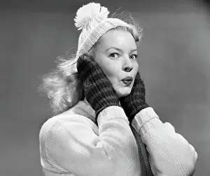 Oldtime Prints: 1950s YOUNG WOMAN PURSING LIPS HANDS COVERING EARS LOOKING AT CAMERA WEARING WINTER WOOL SWEATER MITTENS KNIT CAP