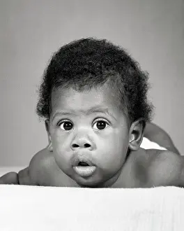 Laying Prints: 1960s AFRICAN-AMERICAN BABY LAYING ON STOMACH FUNNY FACIAL EXPRESSION
