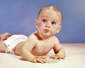 Expressions Prints: 1960s BABY BOY LYING ON HIS STOMACH MAKING FUNNY FACE LOOKING AT CAMERA