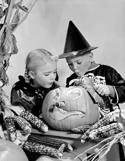 Halloween Prints: 1960S Boy And Girl In Halloween Costumes Looking Into Pumpkin Indoor