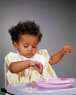 Feed Prints: 1960s INTENT AFRICAN-AMERICAN BABY GIRL SITTING IN HIGH CHAIR LEARNING TO FEED HERSELF PLAYING WITH HER FOOD WITH A
