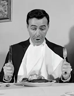 Knife Prints: 1960S Man Sitting At Table Ready To Eat Dinner With Napkin At Neck And Knife & Fork In Air