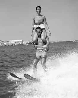 Manly Prints: 1960S Man Water Skiing With Woman In Bathing Suit Riding On Shoulders