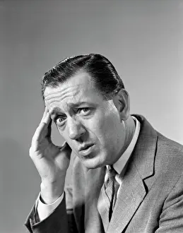 Suffering Prints: 1960S Portrait Man In Suit And Tie With Wrinkled Brow Wincing And Holding Forehead Looking At Camera