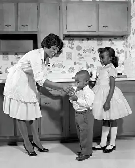 Small Group Of People Prints: 1960S Smiling African American Woman Mother In Apron And Pumps Giving A Glass Of Milk To Son And Daughter With Mary
