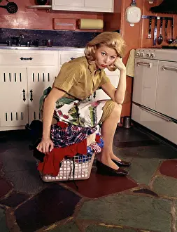 Dreams Prints: 1960S Weary Dejected Woman Housewife Homemaker Sitting On Full Laundry Basket In Kitchen