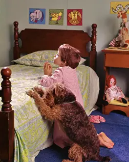 Canines Prints: 1970s 1980s LITTLE RED HAIR GIRL KNEELING IN BEDROOM BESIDE BED SAYING PRAYERS WITH PET WIRE HAIR TERRIER DOG ALONGSIDE