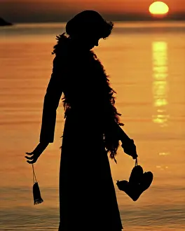 Anonymous Prints: 1970s ANONYMOUS SILHOUETTE PROFILE OF YOUNG WOMAN WEARING FEATHER BOA CARRYING EVENING PURSE AND SHOES WALKING BY