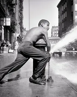 Anonymous Prints: 1970s ANONYMOUS TEENAGE AFRICAN-AMERICAN YOUNG MAN OPENING FIRE HYDRANT AND CREATING COOLING WATER SPRAY NEW YORK CITY