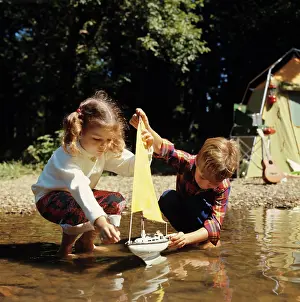 Tent Prints: 1970S Boy Girl At Edge Of Stream Lake With Toy Sail Boat Yellow Sail Tent Guitar Campsite In Background Camping