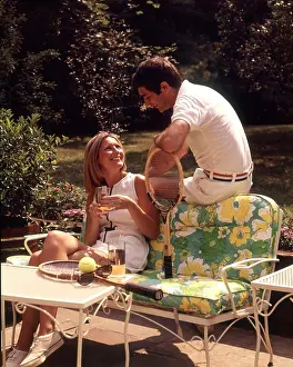 Grownup Prints: 1970s RELAXING COUPLE SITTING ON PATIO FURNITURE WITH DRINKS BOTH WEARING TENNIS TOGS AFTER PLAYING