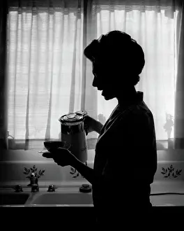 Beginning Prints: 1970s SILHOUETTED ANONYMOUS WOMAN HOUSEWIFE SPEAKING WHILE POURING FIRST CUP OF MORNING COFFEE IN KITCHEN