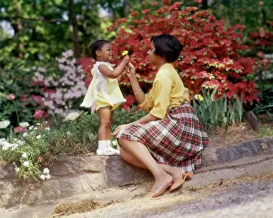 Oldtime Prints: 1970s SMILING AFRICAN AMERICAN WOMAN AND LITTLE GIRL OUTDOORS NEAR SPRING FLOWERS DAUGHTER GIVING YELLOW FLOWER TO