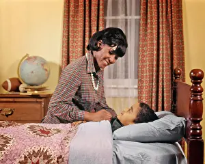 Sons Prints: 1970s SMILING AFRICAN AMERICAN WOMAN MOTHER TUCKING GIRL DAUGHTER INTO BED AT NIGHT