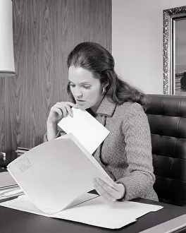 Thoughtful Prints: 1970s WOMAN ADMINISTRATOR INTENTLY FOCUSED ON REVIEWING CONTENTS OF A FILE SEATED AT HER DESK - o3331 HAR001 HARS