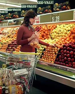 Produce Prints: 1970s WOMAN GROCERY STORE SHOPPING CART SELECTING ORANGES IN PRODUCE DEPARTMENT OF FOOD SUPERMARKET