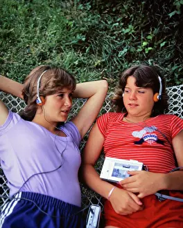Sound Prints: 1980s TWO TEEN GIRLS LYING ON HAMMOCK LISTENING FOAM HEADPHONES TO SOUNDS MUSIC RECORDED CASSETTE ON PORTABLE MEDIA