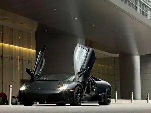 Hood Prints: Front 3/4 static view of a matte black 2010 Lamborghini Murcielago LP 670-4 parked in front of a building with gull