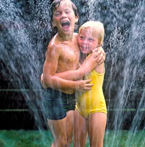 Recreation Prints: Adolescent boy and girl wearing their bathing suits playing outside in the water sprinkler