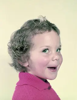 Expressive Prints: Adorable toddler with curly hair in a pink sweater smiling playfully
