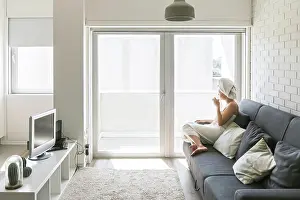 Balcony Prints: Adult relaxed woman enjoying life while resting on sofa and having hot drink after shower in own cozy apartment