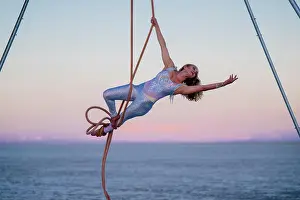 Talent Prints: Aerial performer in shiny outfit elegantly poses on rope against ocean and sunset sky