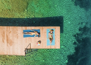 Jetty Prints: Aerial view of two attractive women sunbathing on wooden pontoon in Panagopoula, Greece