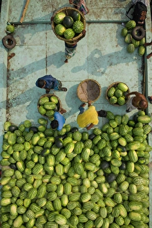 Foodstuff Prints: Aerial view of farmer working together onboard of a wooden boat unloading watermelons along Buriganga river in Dhaka