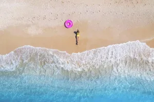 Adriatic Prints: Aerial view of the lying beautiful young woman with pink swim ring on the sandy beach near sea with waves at sunset