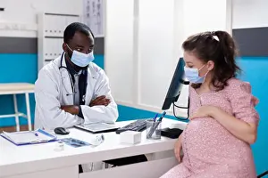 Examination Prints: African american doctor talking to pregnant woman at desk