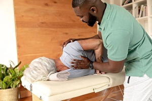 Therapist Prints: African american male physiotherapist giving back massage therapy to caucasian senior woman at home