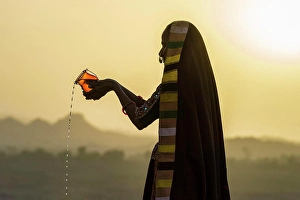 Headscarf Prints: Ahir Woman in traditional colorful cloth pouring water at sunset