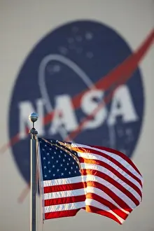 American flag in foreground and large NASA insignia on the side of the Vehicle Assembly Building (VAB)