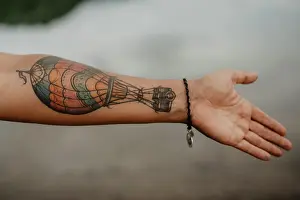 Anonymous Prints: Anonymous female showing arm with hot air balloon tattoo over tranquil surface of lake in countryside