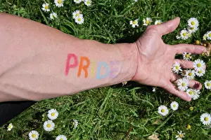 Union Prints: arm of a man painted with the word pride in the colors of the lgtbi flag stretched over a lawn full of daisies