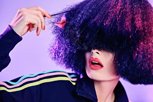 Contemporary Prints: Astonished female in stylish sportswear inspecting fake hair under bright illumination against violet background