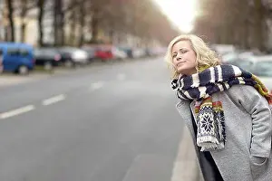 Chic Prints: Attractive blond woman in warm stylish winter fashion waiting for a cab or a lift peering anxiously down an urban