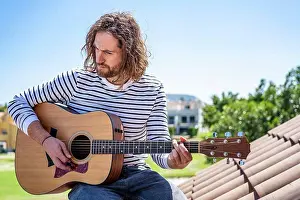 Expressive Prints: Attractive man with long hair playing acoustic guitar outdoors