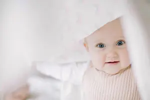 Playtime Prints: Baby girl looking at the camera while playing under a blanket