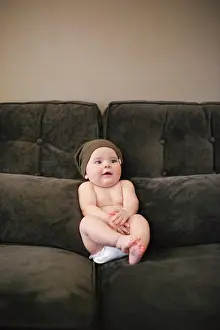 Beginnings Prints: A baby sitting propped up on a sofa wearing a diaper