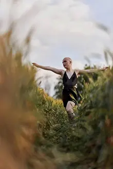 Bald Prints: Bald transgender woman in black dress walking with arms outstretched in agricultural field