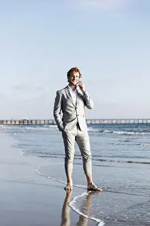 Business Travel Prints: Barefoot businessman talking on smart phone on sunny ocean beach, Los Angeles, California