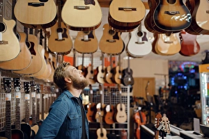 Audio Prints: Bearded young guy choosing acoustic guitar in music store