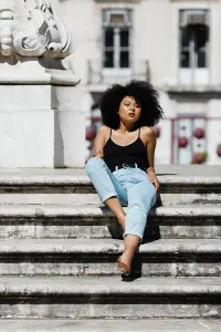 Curly Prints: Beautiful ethnic woman in jeans and tank top relaxing and sunbathing on stone stairs against urban background